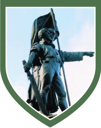 bronze statue of John Kelly holding a flag and sword, pointing forward with an outstretched arm, framed within a green shield border, featured at the National 1798 Rebellion Centre, Enniscorthy.