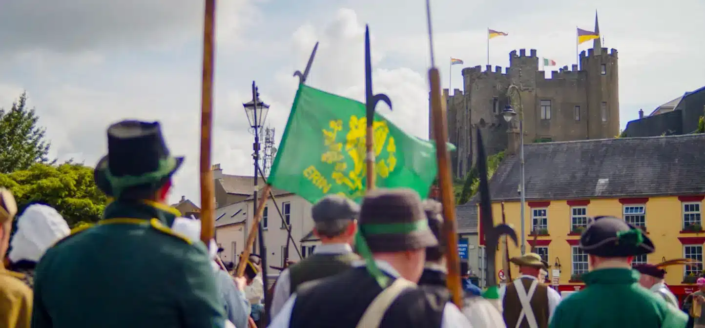 Display at the National 1798 Rebellion Centre, Enniscorthy, showing a replica cannon on wooden wheels, surrounded by muskets, a figure in red uniform and a mural of reenactors dressed as 1798 rebels.