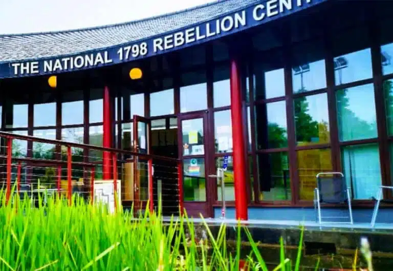 Entrance of the National 1798 Rebellion Centre in Enniscorthy, featuring curved modern architecture with glass panels, red pillars and greenery in the foreground.