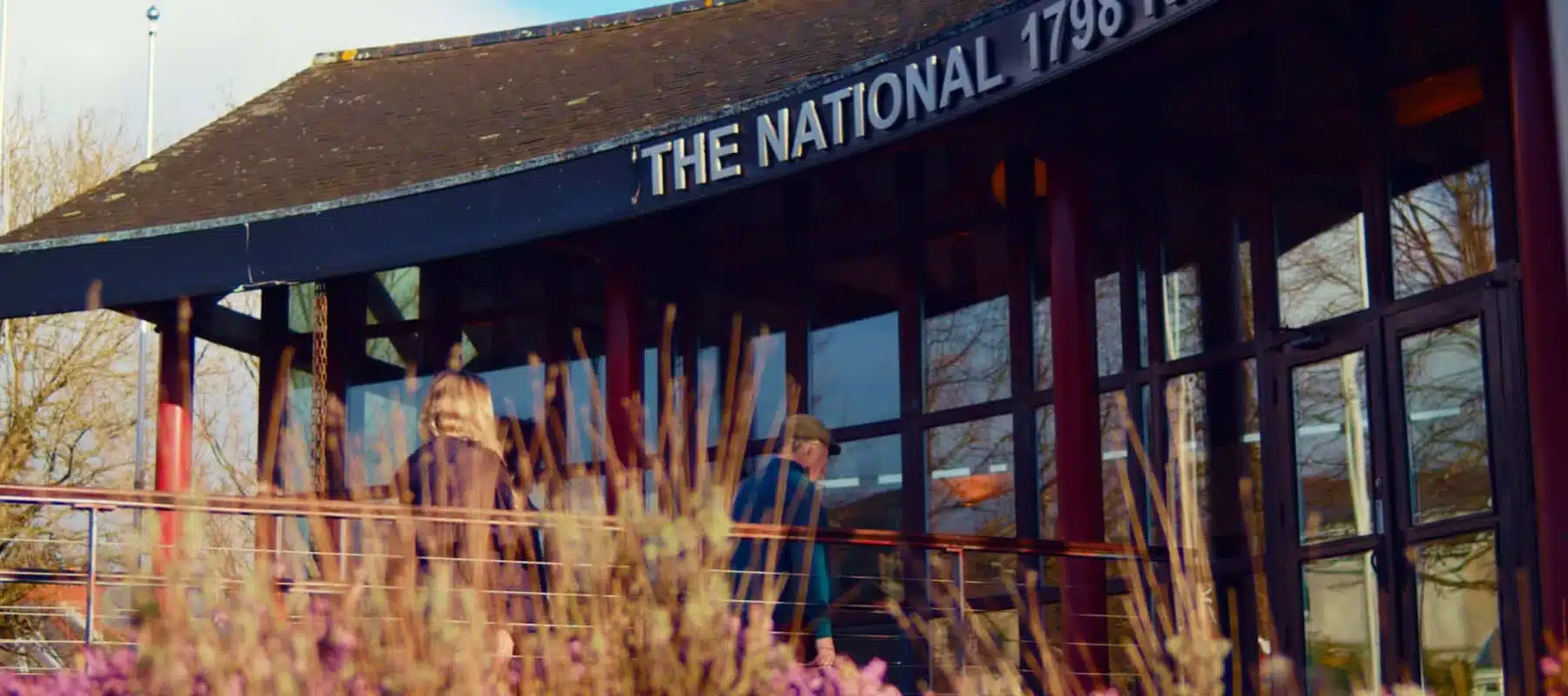 Entrance of the National 1798 Rebellion Centre in Enniscorthy, featuring curved modern architecture with glass panels, red pillars and greenery in the foreground.